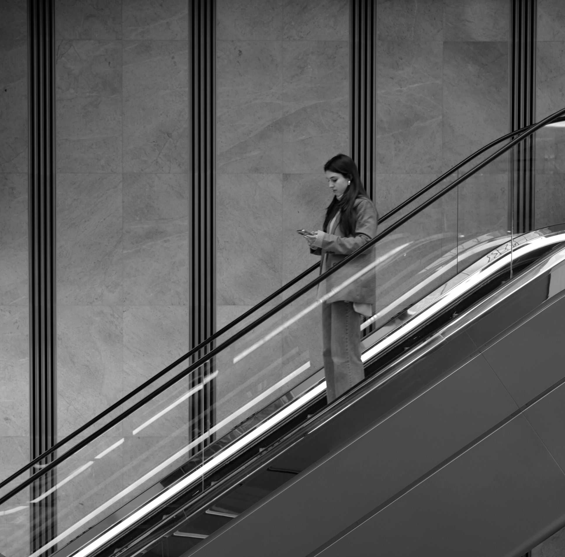 Girl in escalator looking at her phone in black and white