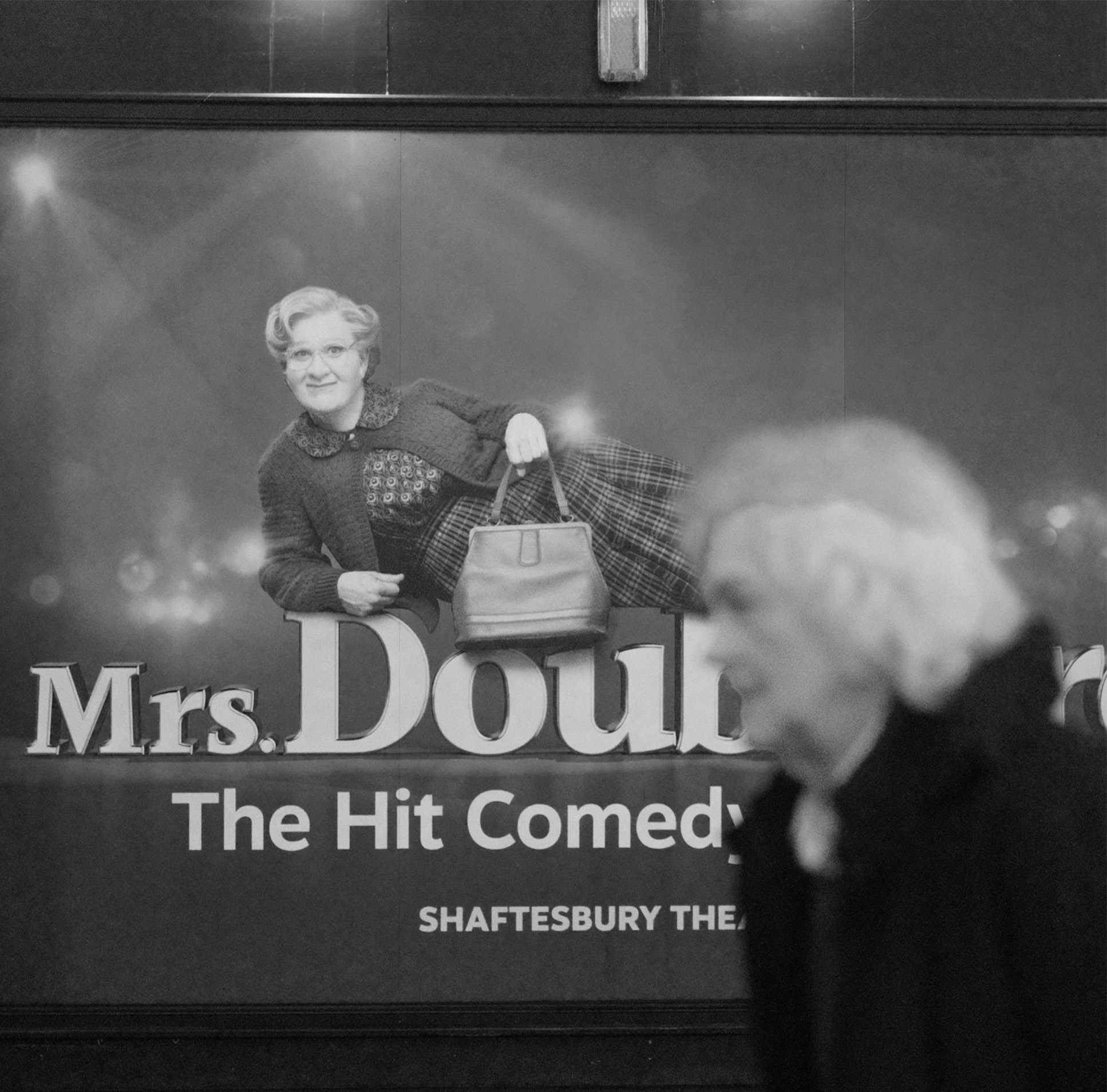 Woman walking past a movie poster in black and white